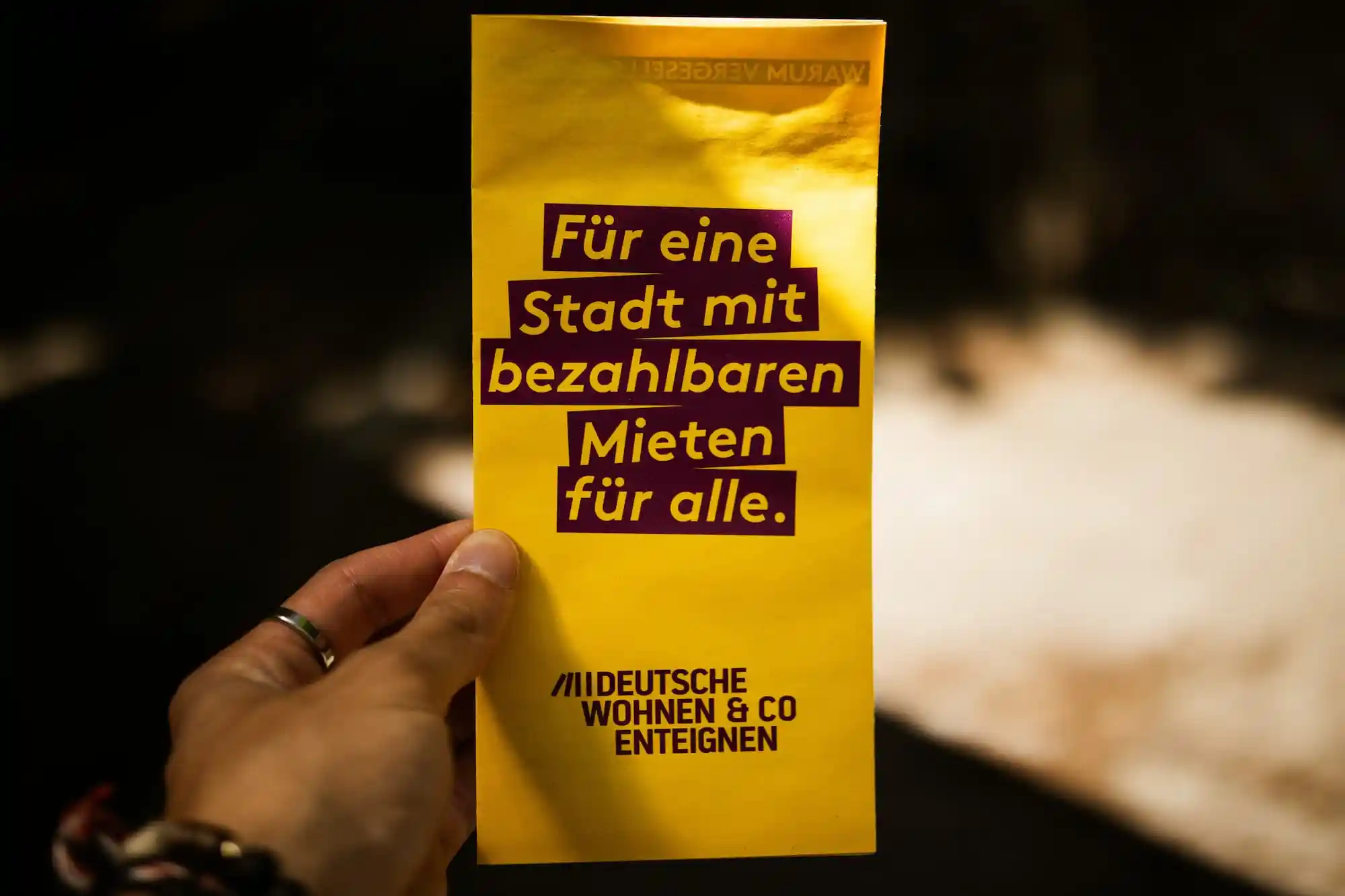 Eine Hand hält einen Flyer der Initiative Deutsche Wohnen & Co enteignen. Auf dem Flyer steht: „Für eine Stadt mit bezahlbaren Mieten für alle.“